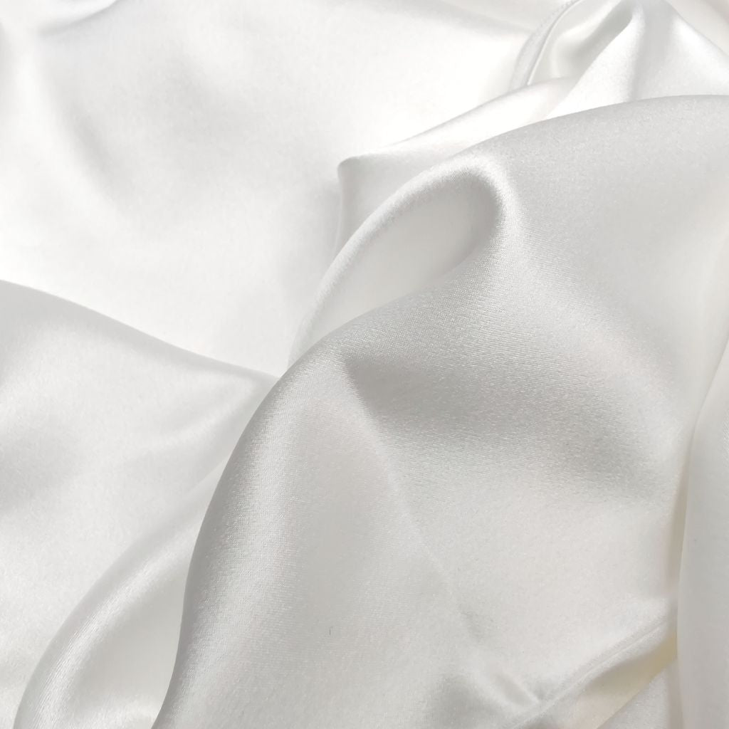 Close-up van de gladde, glanzende stof van een witte satijnen kussensloop van moerbeizijde.