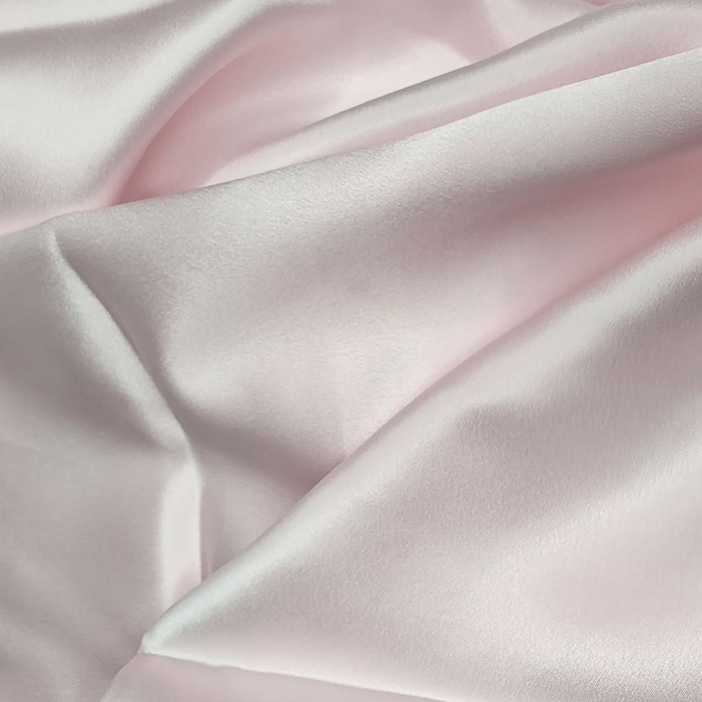Close-up van de gladde, glanzende stof van een roze satijnen kussensloop van moerbeizijde.